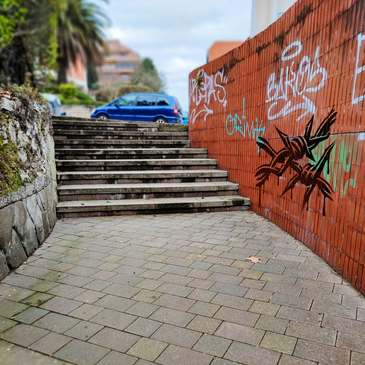 Beside outdoor stairs, the Dripping Barbed Wire Graffiti Stencil adds bold black street art to a red brick wall.