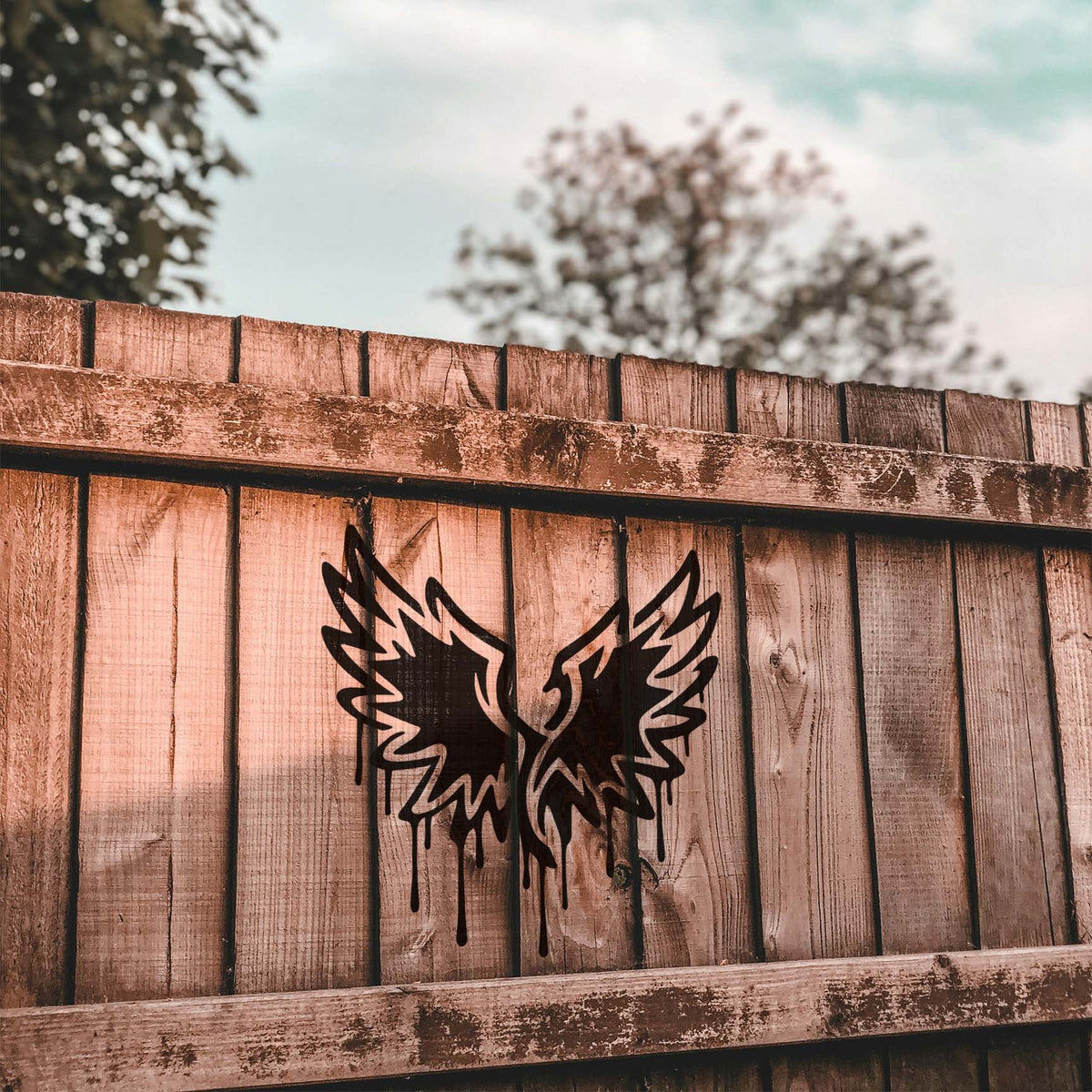 Across rustic wooden planks, the Graffiti Wings Stencil reveals sharp feathers and dramatic black paint drips.