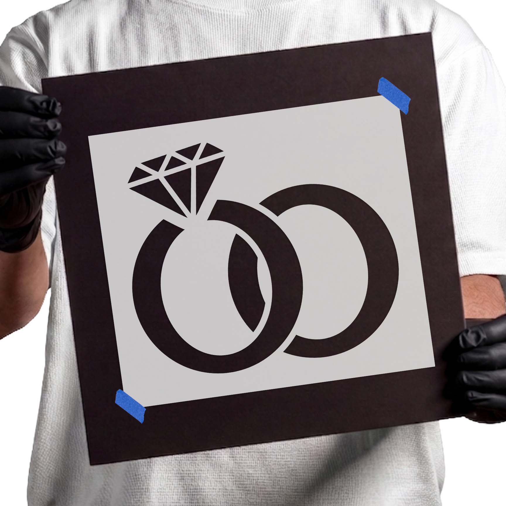 Gloved hands holding Interlocking Wedding Rings stencil taped to black cardboard