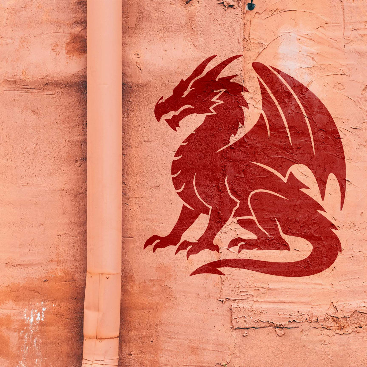 On a weathered peach wall, the Majestic Sitting Dragon Silhouette Stencil reveals a horned dragon in deep red.