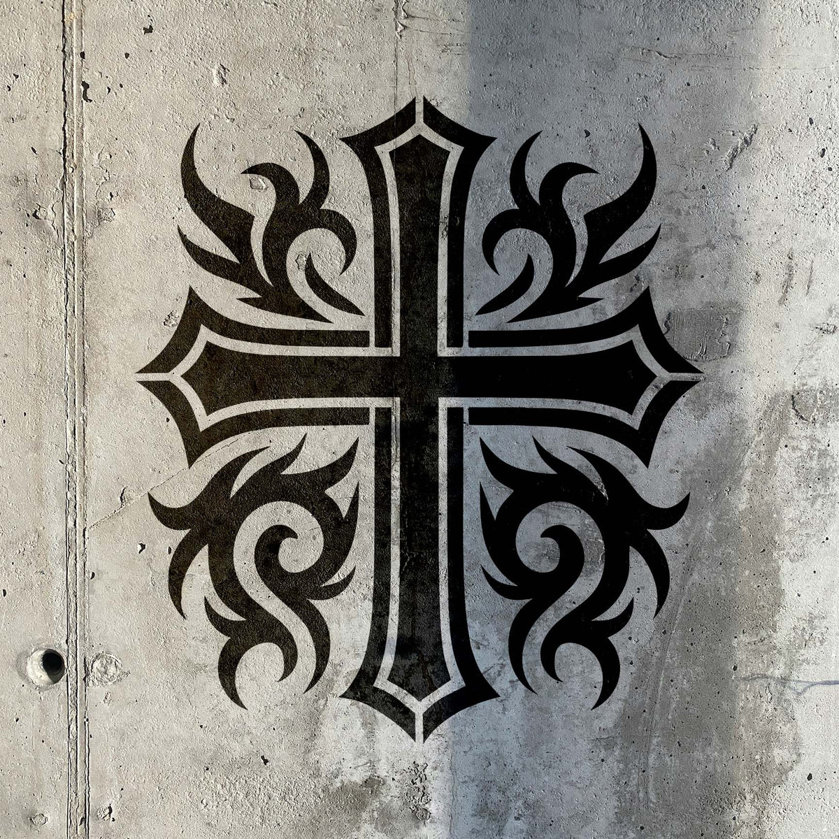 Bold Ornate Tribal Cross Stencil with sweeping tribal details painted black on a concrete wall