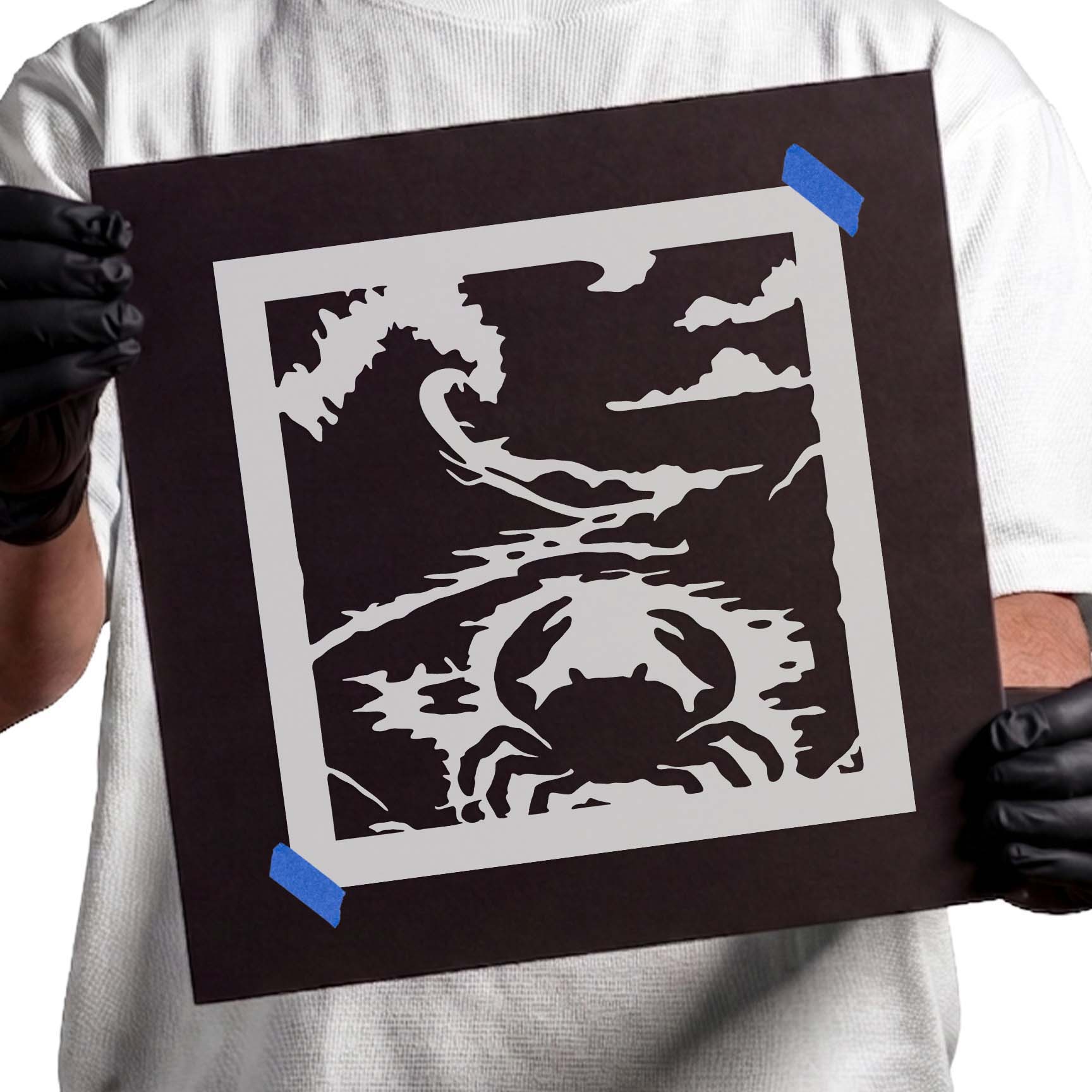 Gloved hands holding Seashore Crab Stencil taped to black cardboard