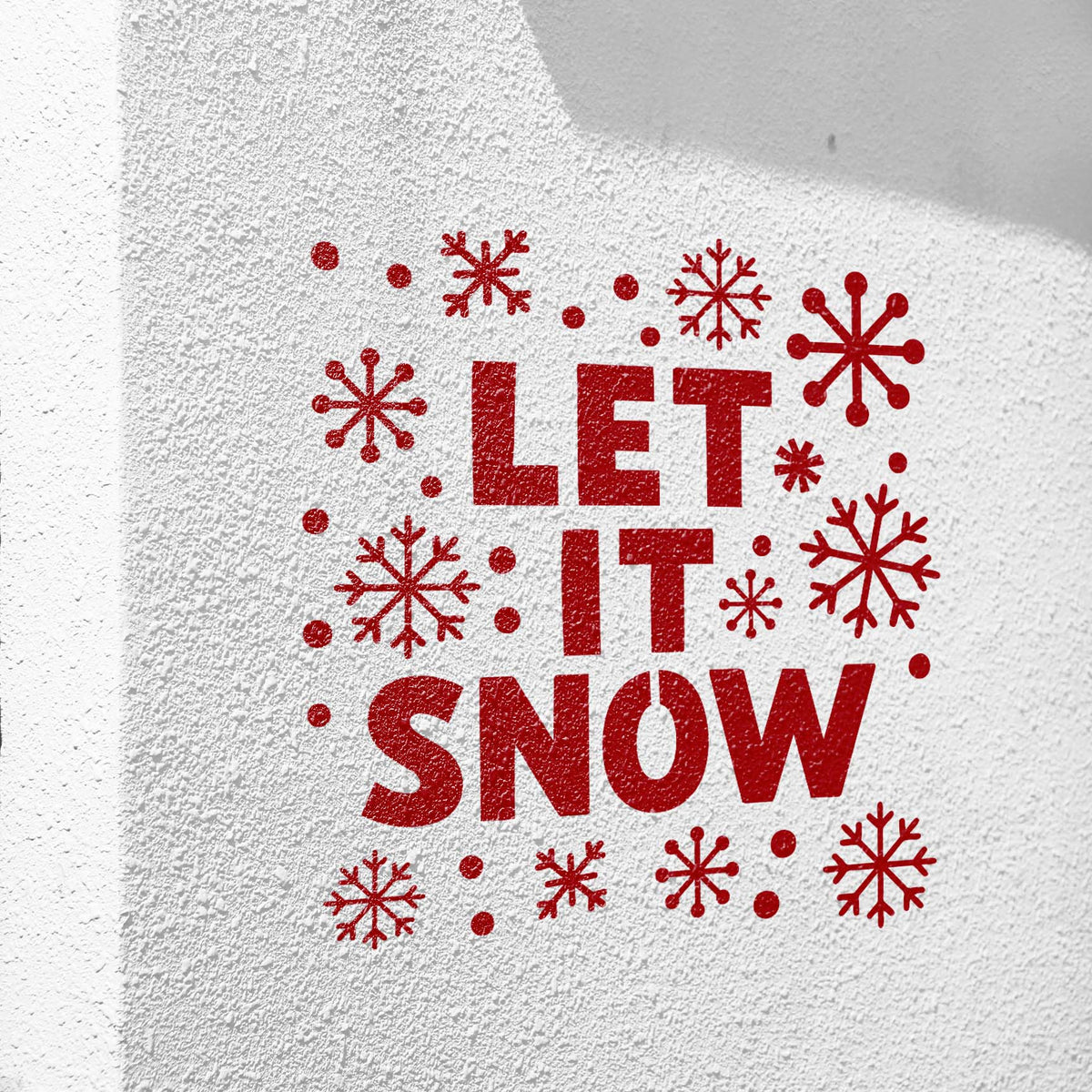 Bright red Snowflake Let It Snow Stencil stands out on a textured white wall with winter flakes.