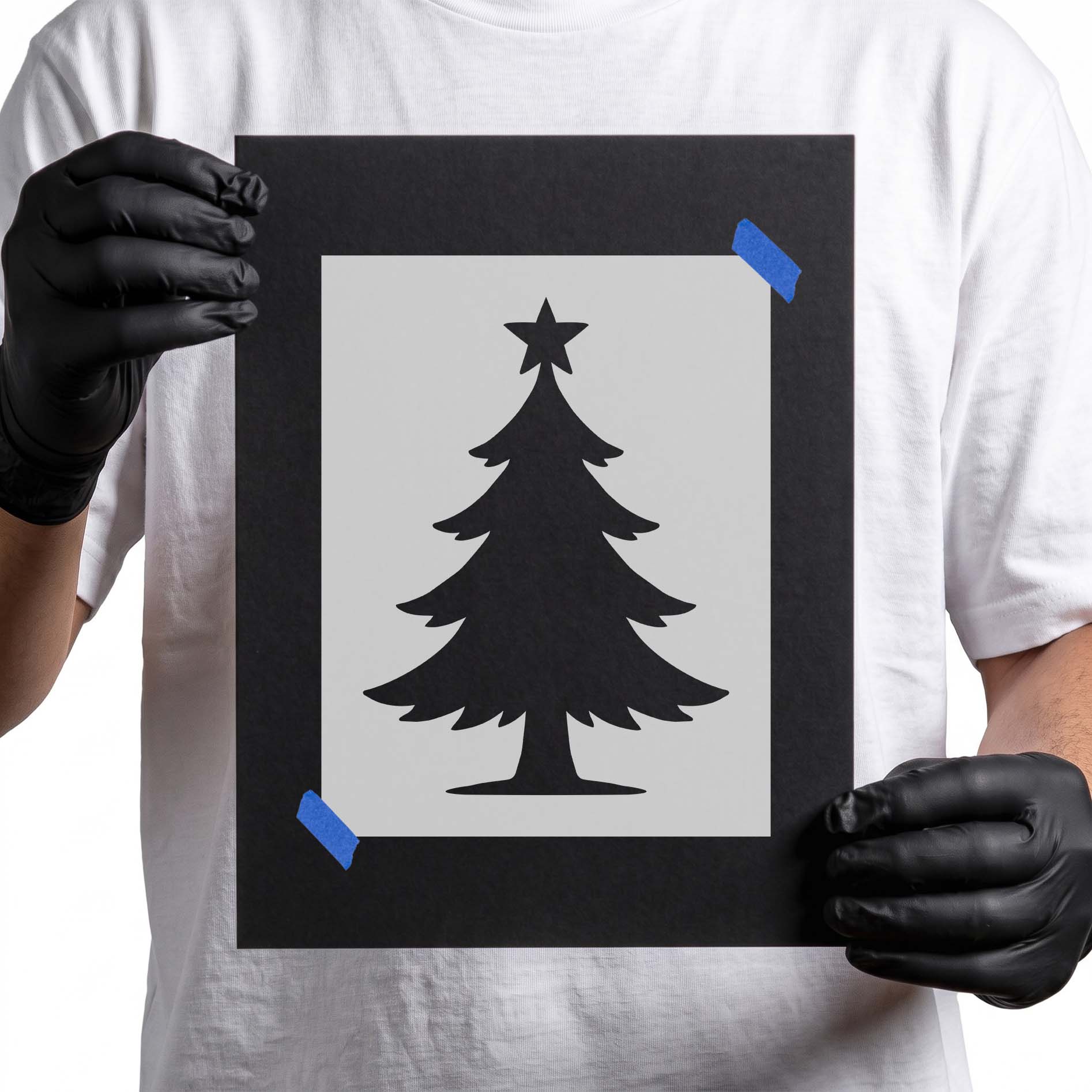 Gloved hands holding Star Topped Christmas Tree stencil taped to black cardboard