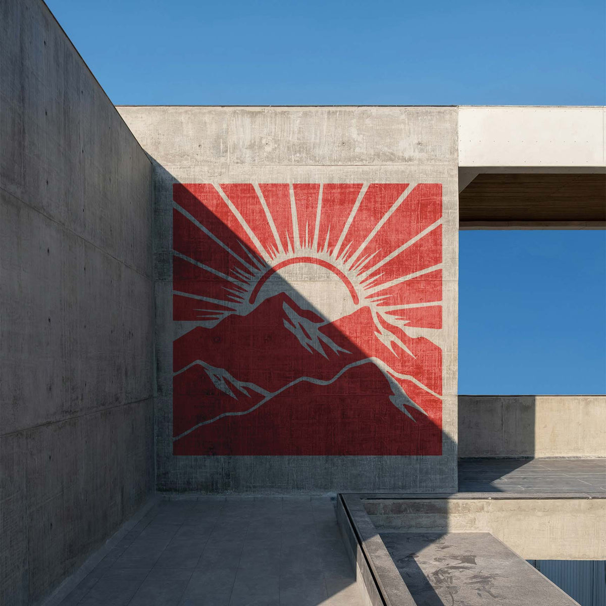 Across a modern concrete wall, the Sunrise Mountain Landscape Stencil reveals red mountains and a rising sun.