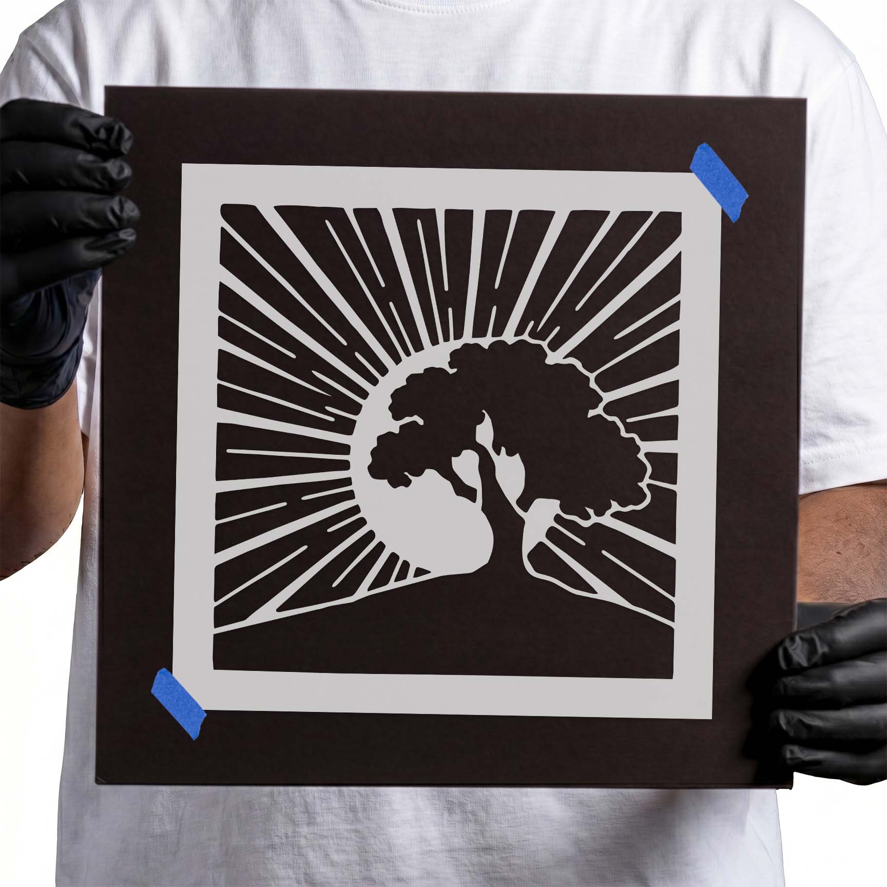 Person holding Sunrise Tree Silhouette Stencil taped to black cardboard