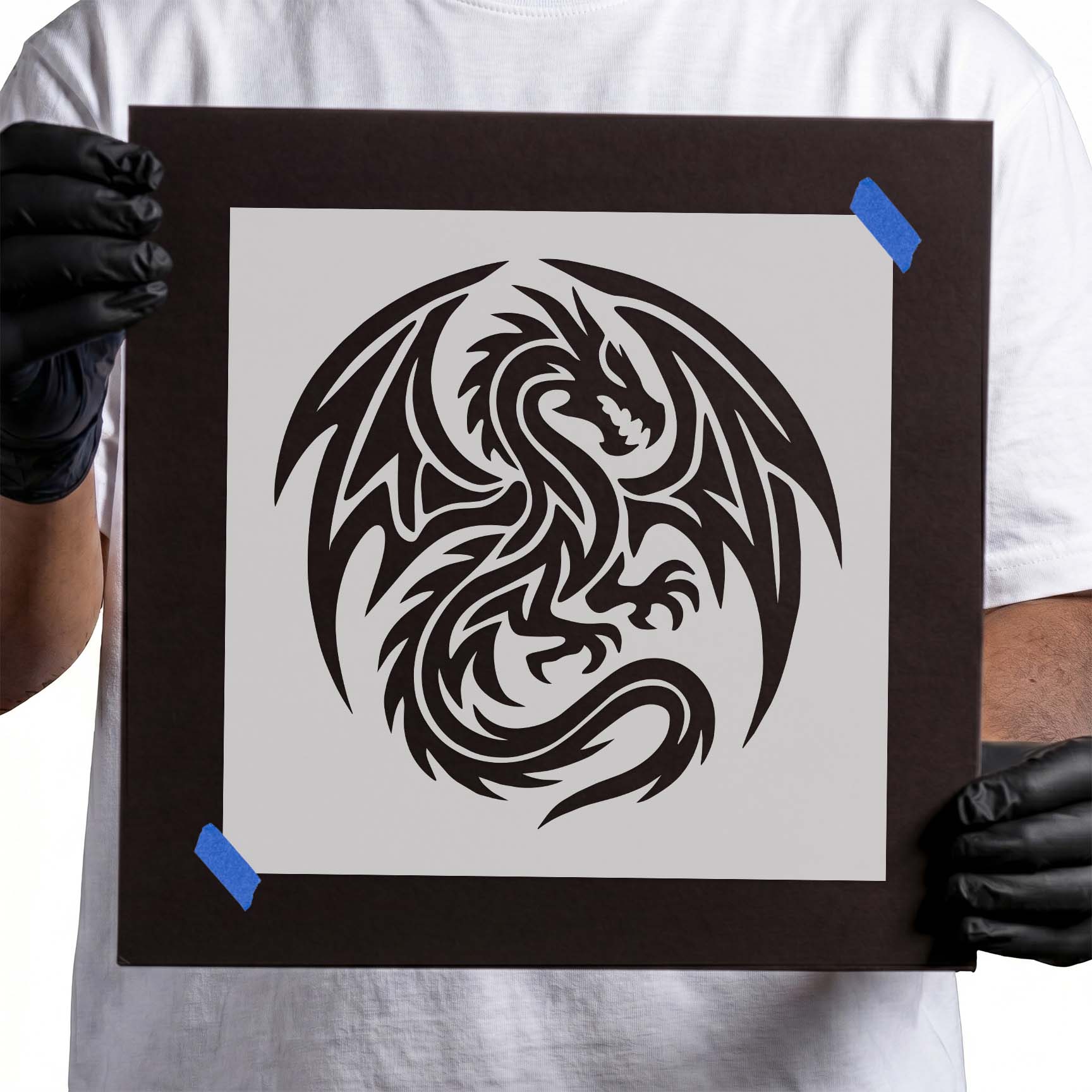 Person holding Tribal Winged Dragon Stencil taped to black cardboard