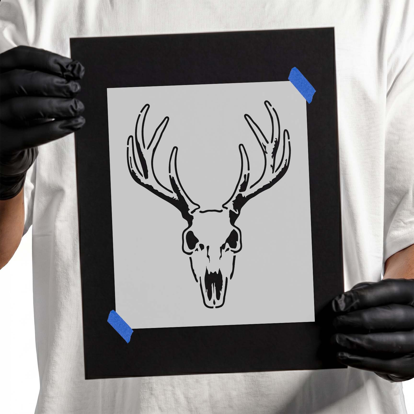 Gloved hands holding Whitetail Buck Skull Stencil taped to black cardboard