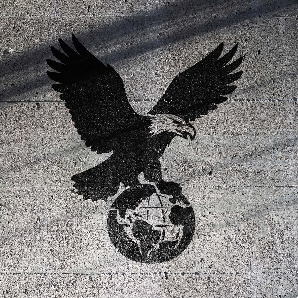 Black American Eagle Perched on Globe Stencil spreads its wings over a globe on a rugged concrete wall.