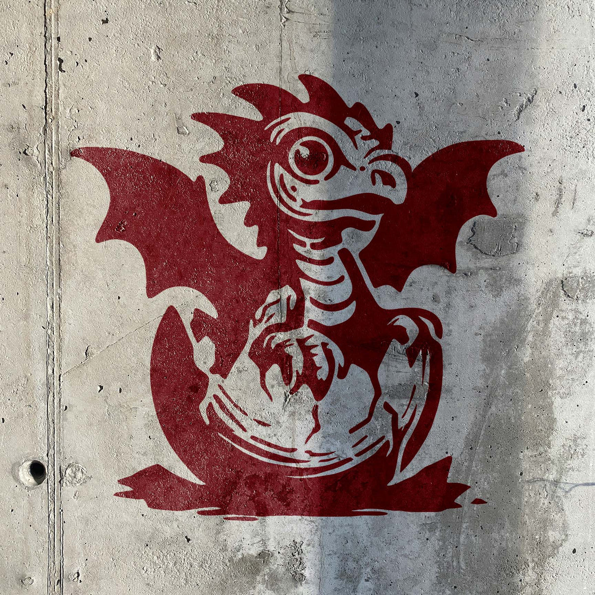 A playful Baby Dragon Hatching Stencil in deep red shows a winged dragon emerging from an egg on concrete.