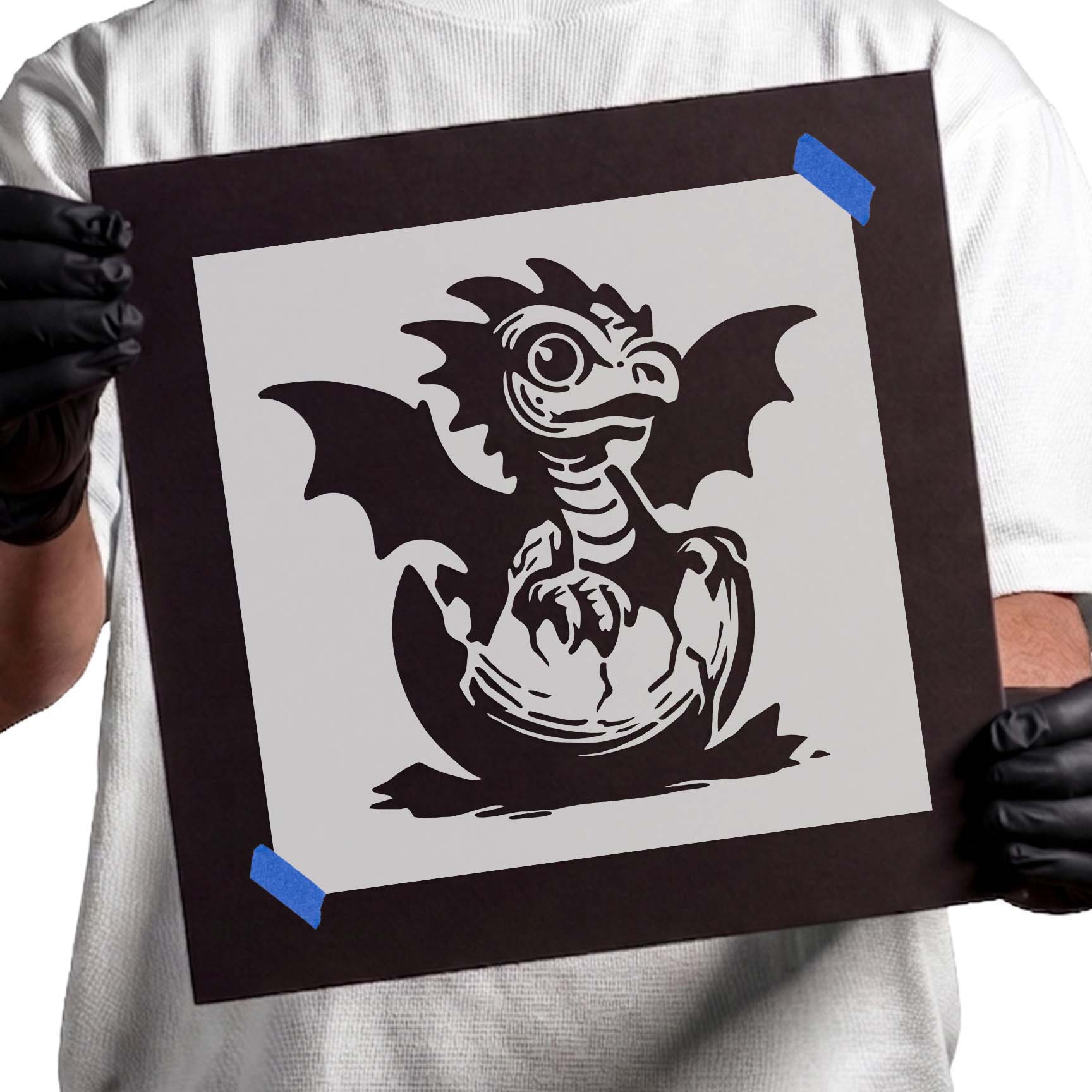 Gloved hands holding Baby Dragon Hatching Stencil taped to black cardboard