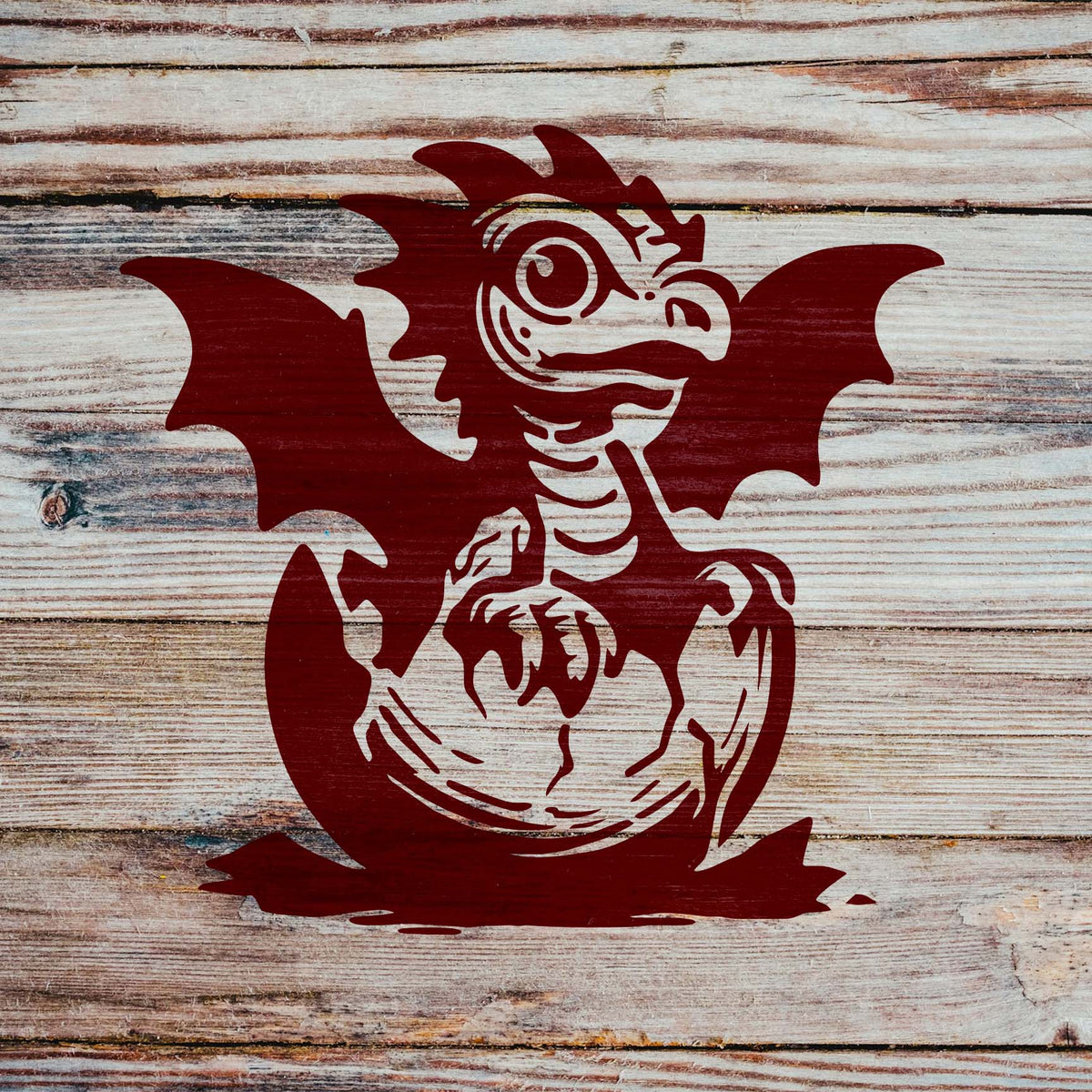 Rustic wooden planks feature the Baby Dragon Hatching Stencil, depicting a wide-eyed dragon breaking from its shell.