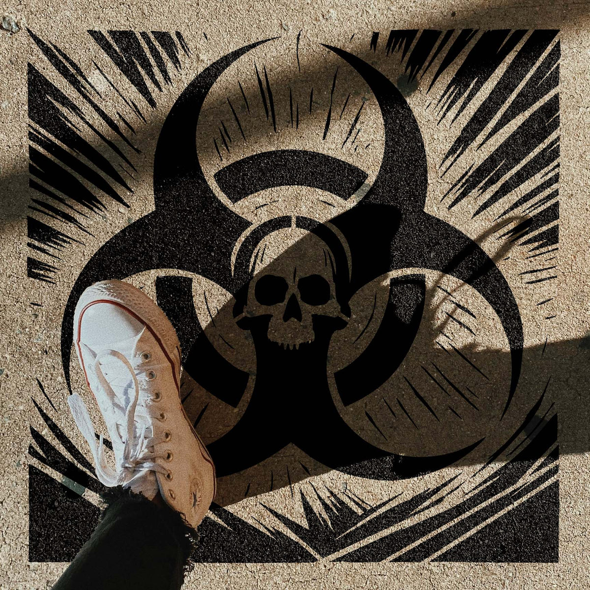 Biohazard Skull Emblem Stencil appears on rough concrete beside a white sneaker and shadows