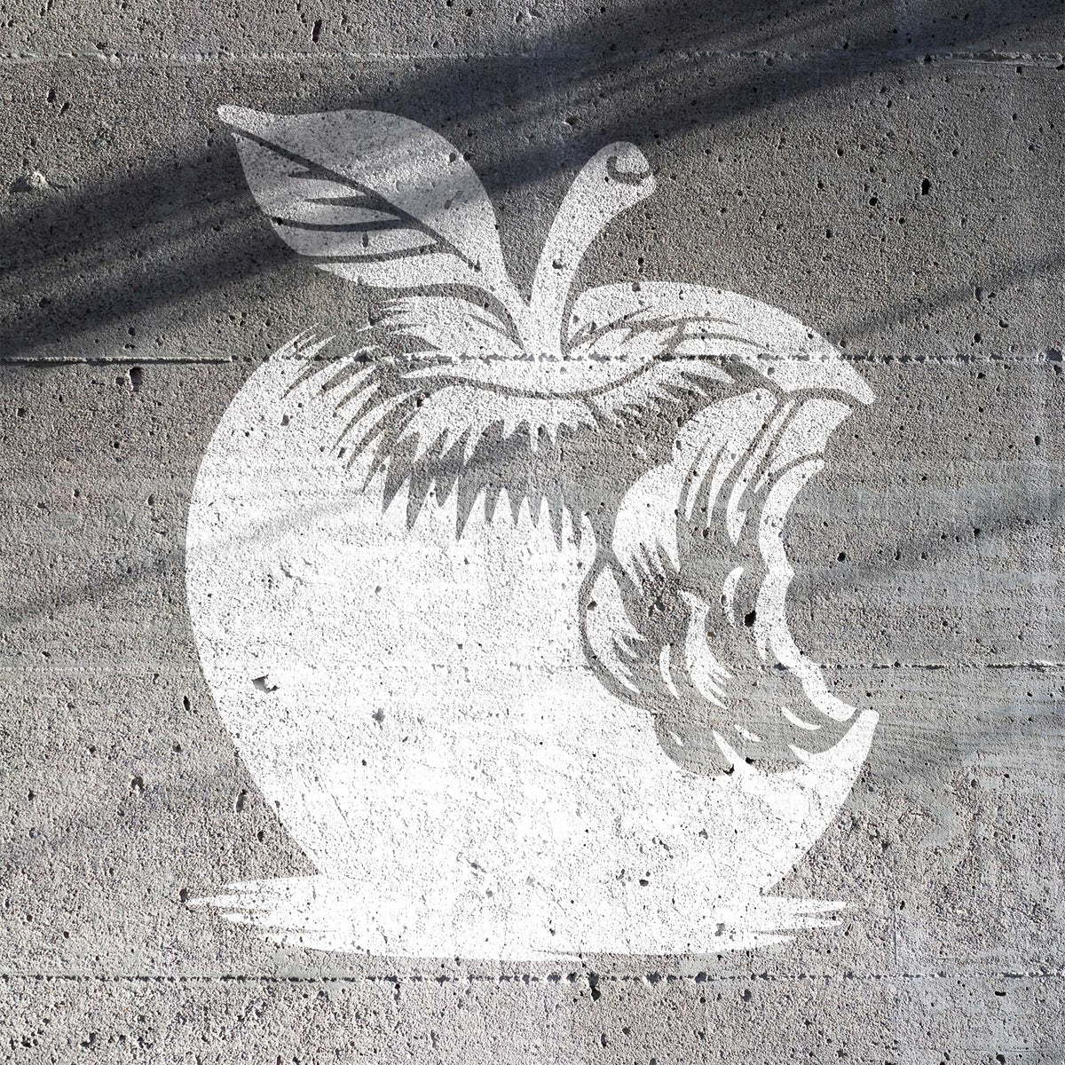 Bitten Apple Stencil painted in white on a gray concrete wall with a distressed finish.