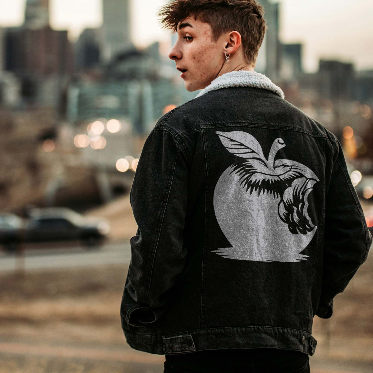 On a black jacket, the Bitten Apple Stencil stands out in white against a city backdrop.