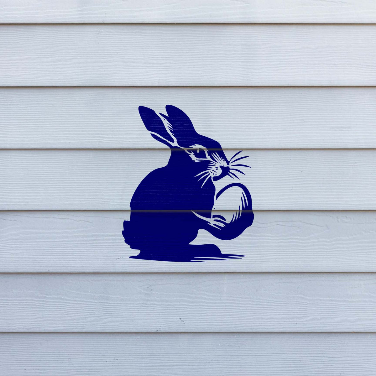 Set against white siding, the Bunny Holding Easter Egg Stencil features a blue rabbit holding an egg.