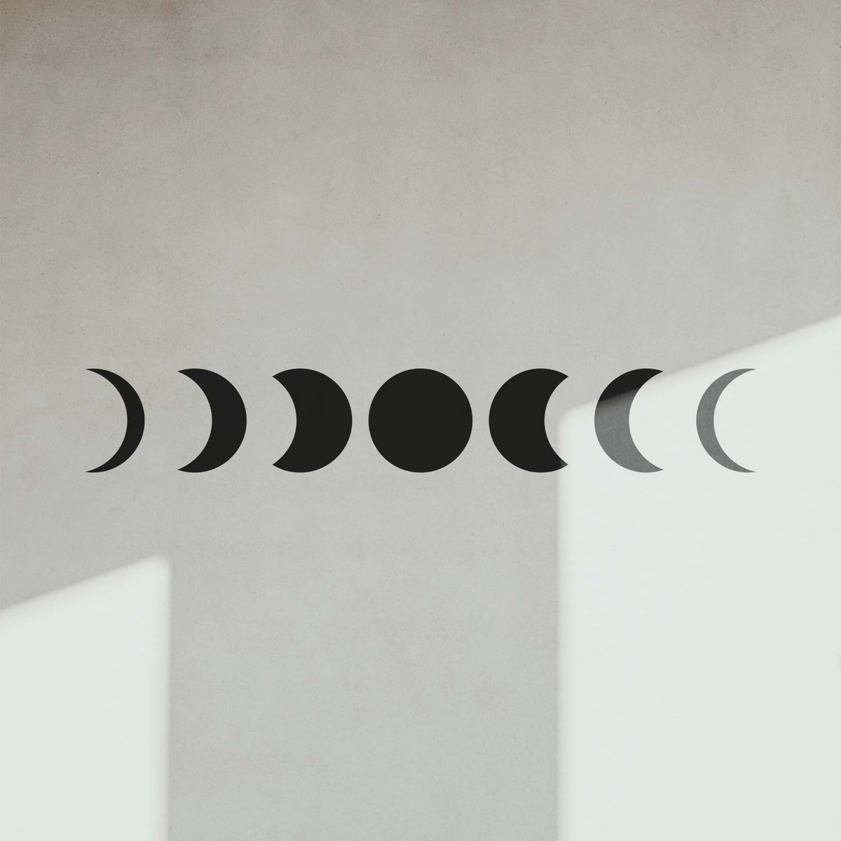 Across a sunlit white wall, the Celestial Moon Phase Border Stencil traces seven lunar shapes in black.