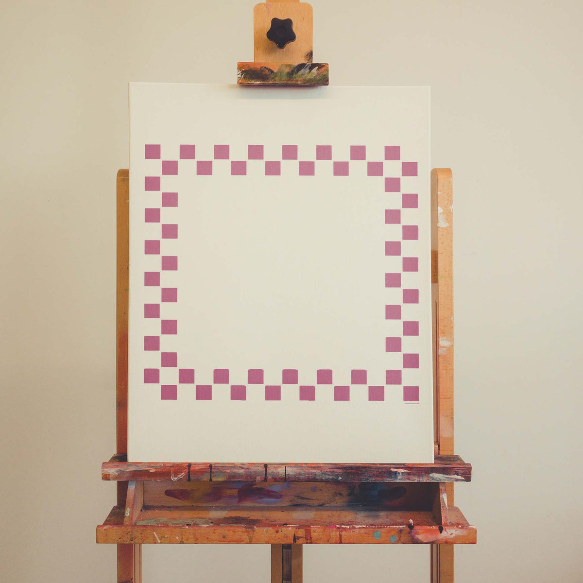 A playful pink Checkerboard Border Frame Stencil outlines a blank canvas with neat squares.