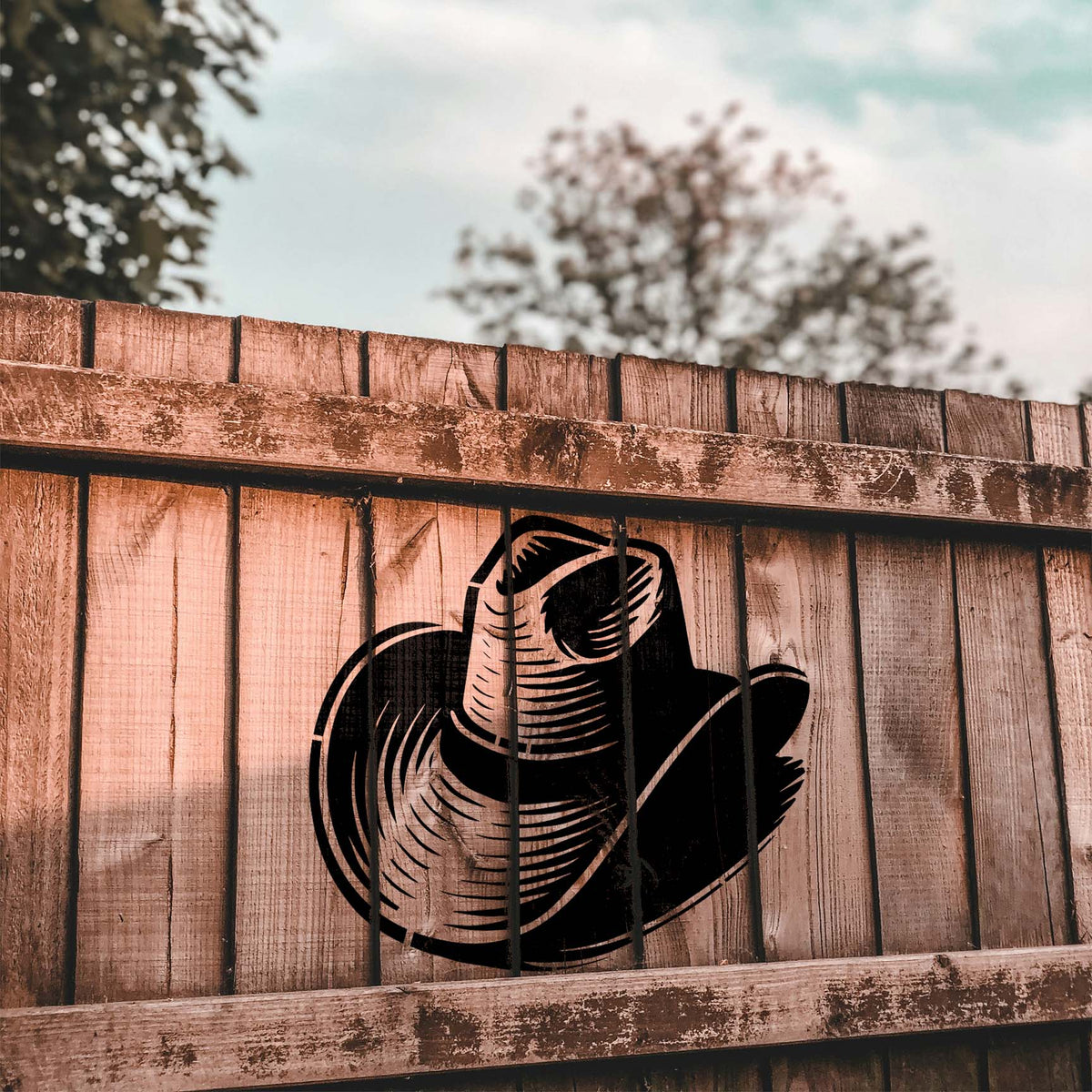 Painted on a rustic wooden fence, the Classic Cowboy Hat Stencil features a bold black hat with textured lines.