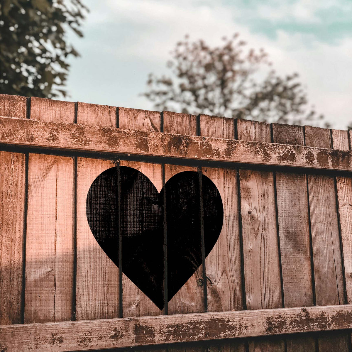 A bold black Classic Heart Stencil stands out against the natural grain of a rustic outdoor wooden fence.