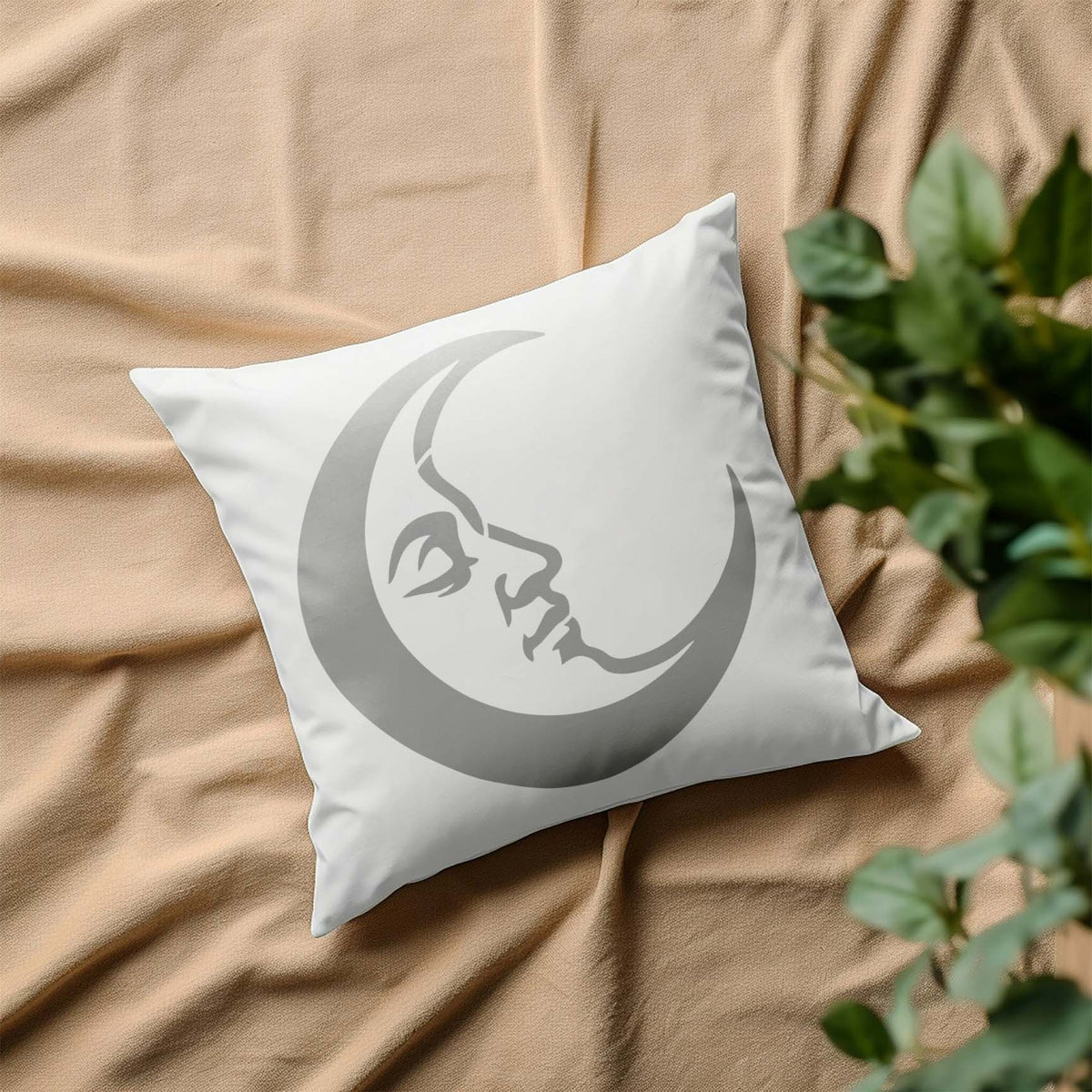 A dreamy silver Crescent Moon Face Stencil lends celestial charm to a white pillow on beige fabric.