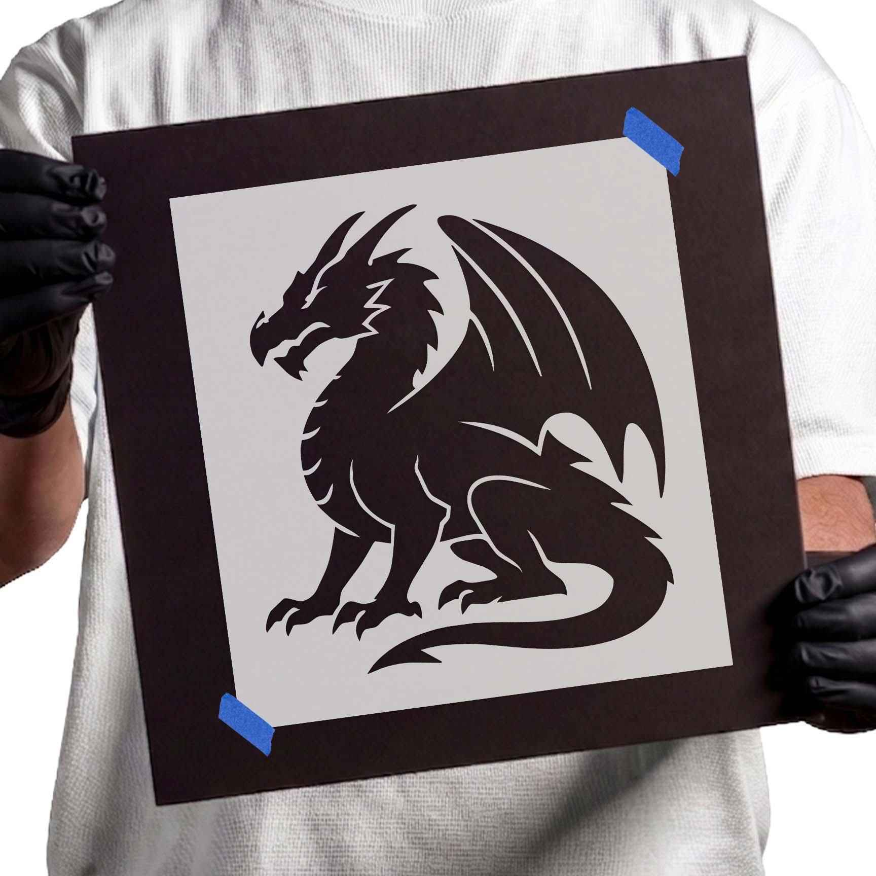 Person holding Majestic Sitting Dragon Silhouette Stencil taped to cardboard