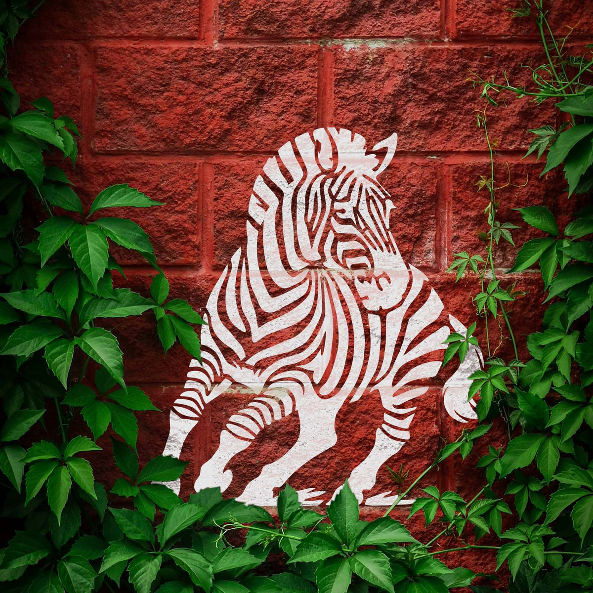 Striking running zebra stencil painted white against a leafy red brick wall