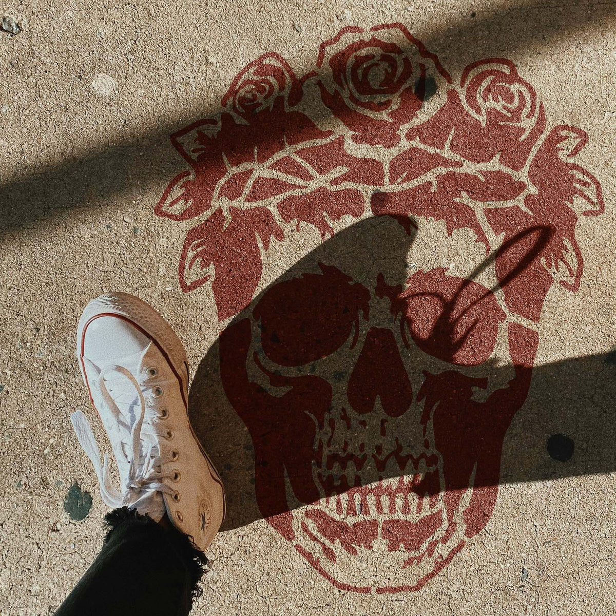 Floral Skull with Rose Crown Stencil painted red on pavement beside a sneaker in sunlight