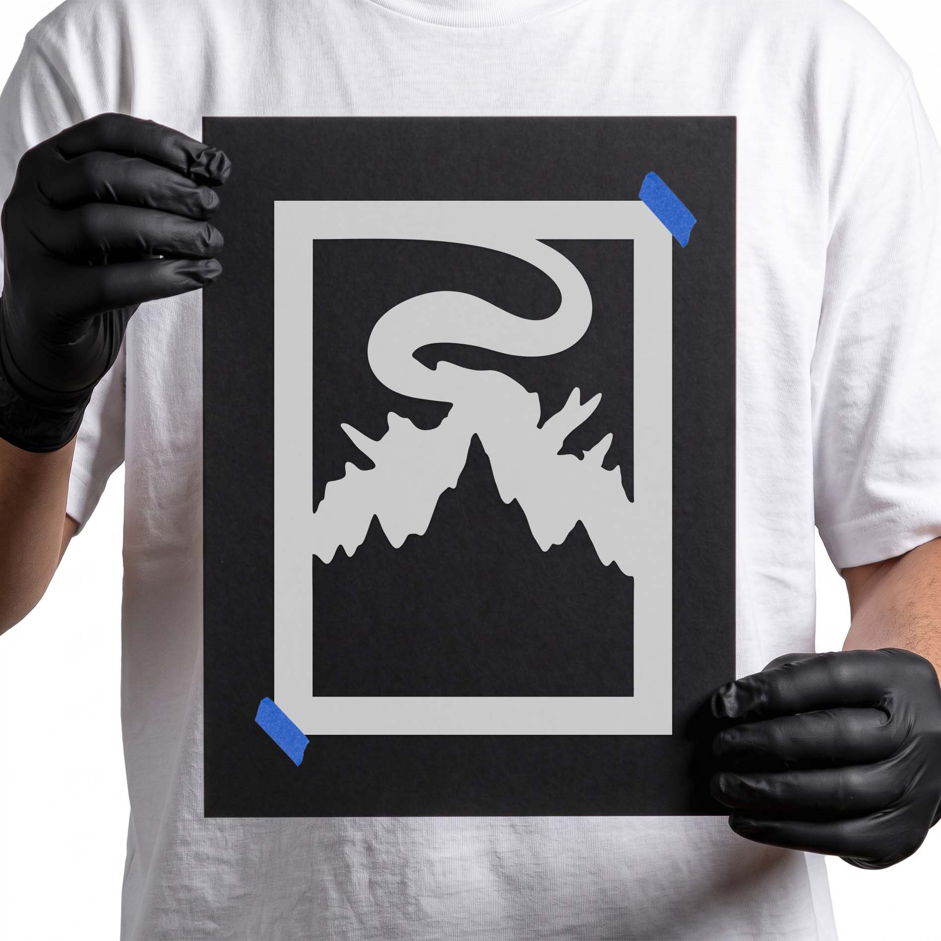 Gloved hands holding Foggy Mountain Landscape Stencil taped to black cardboard