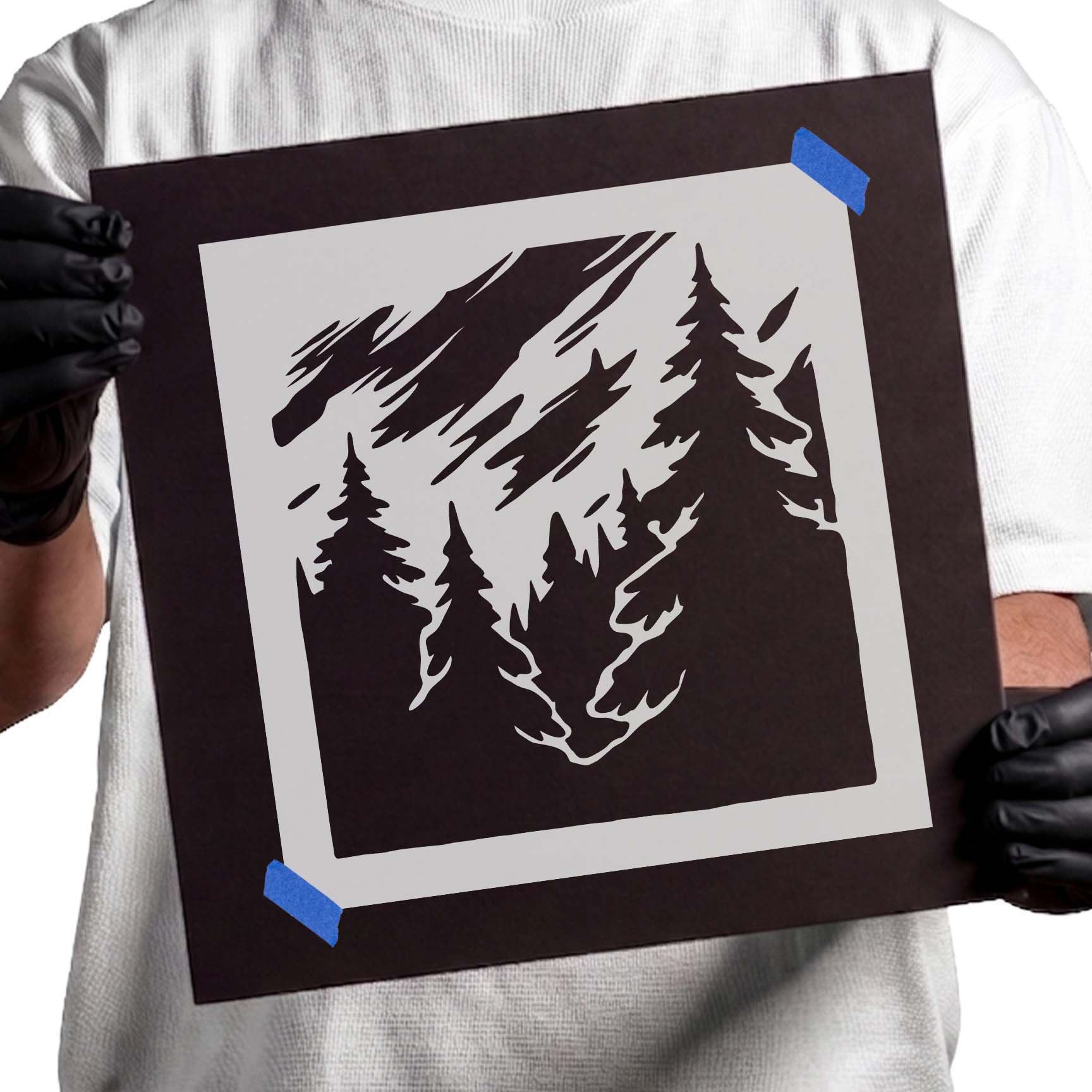 Person holding Misty Pine Forest Stencil taped to black cardboard