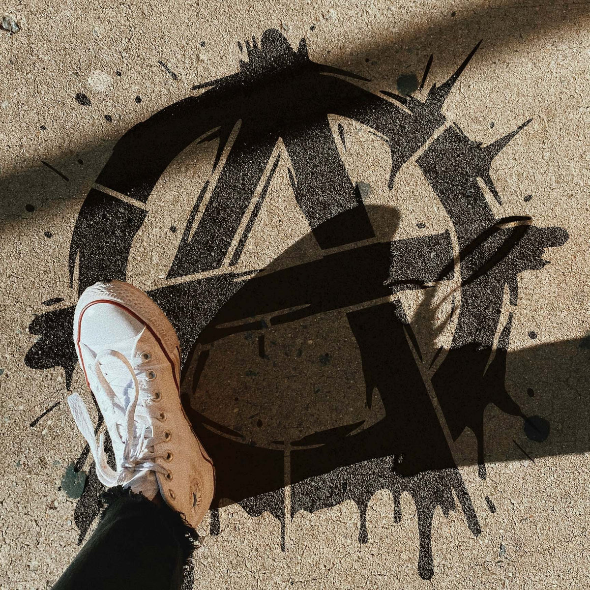 Across sunlit pavement, the Graffiti Anarchy Symbol Stencil reveals a distressed circle-A with dark paint drips.