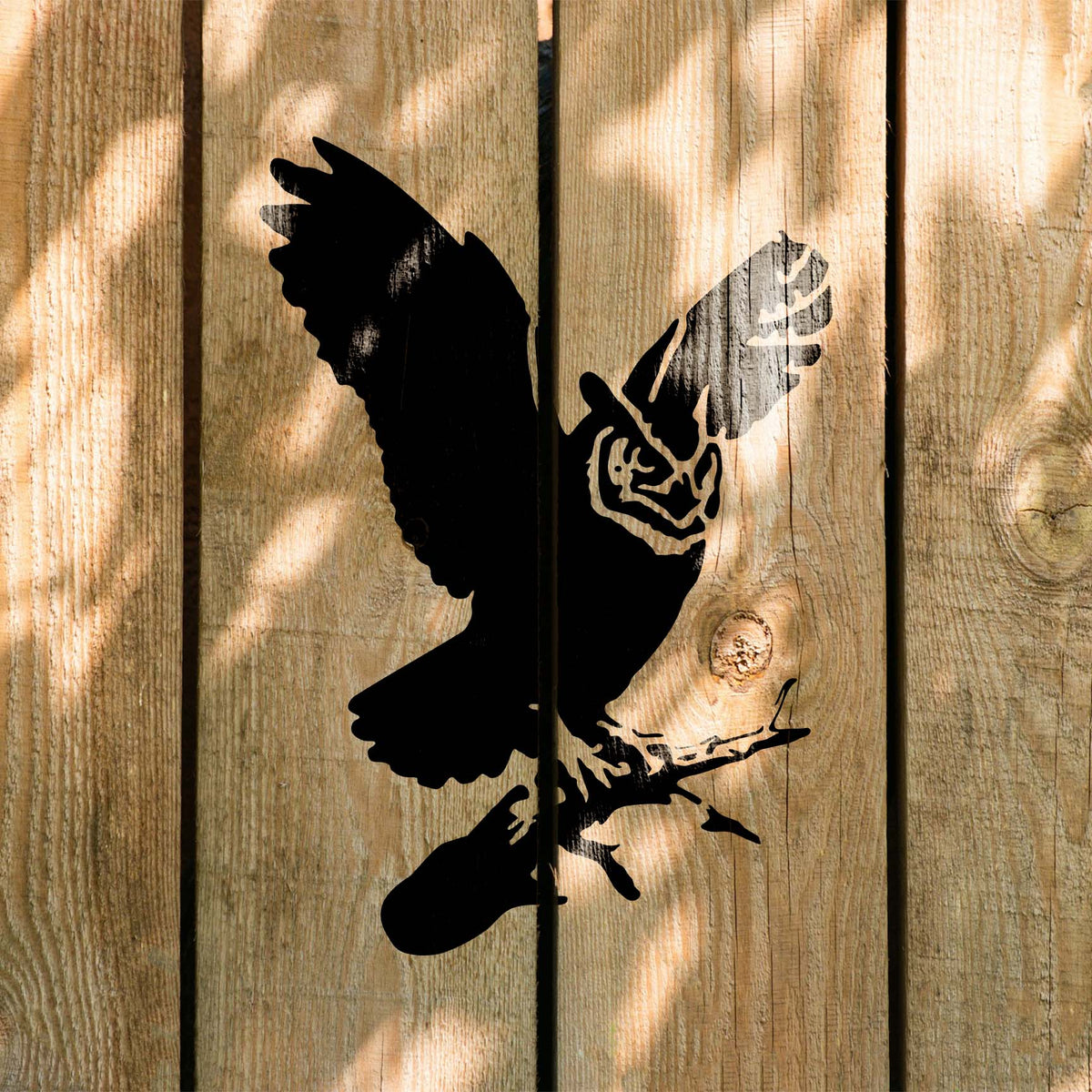 Great Horned Owl Stencil painted in black on a sunlit wooden fence with soft leaf shadows.