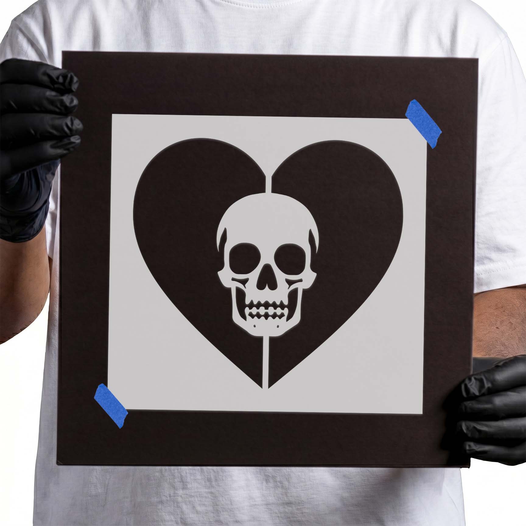 Gloved hands holding Gothic Heart Skull Stencil taped to black cardboard