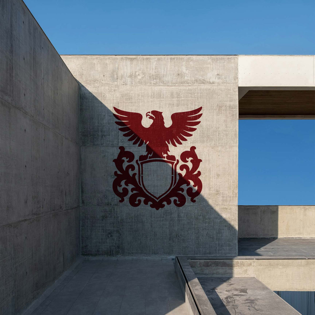 A red Heraldic Eagle Shield Crest Stencil adorns a concrete wall with spread wings and ornate scrollwork.