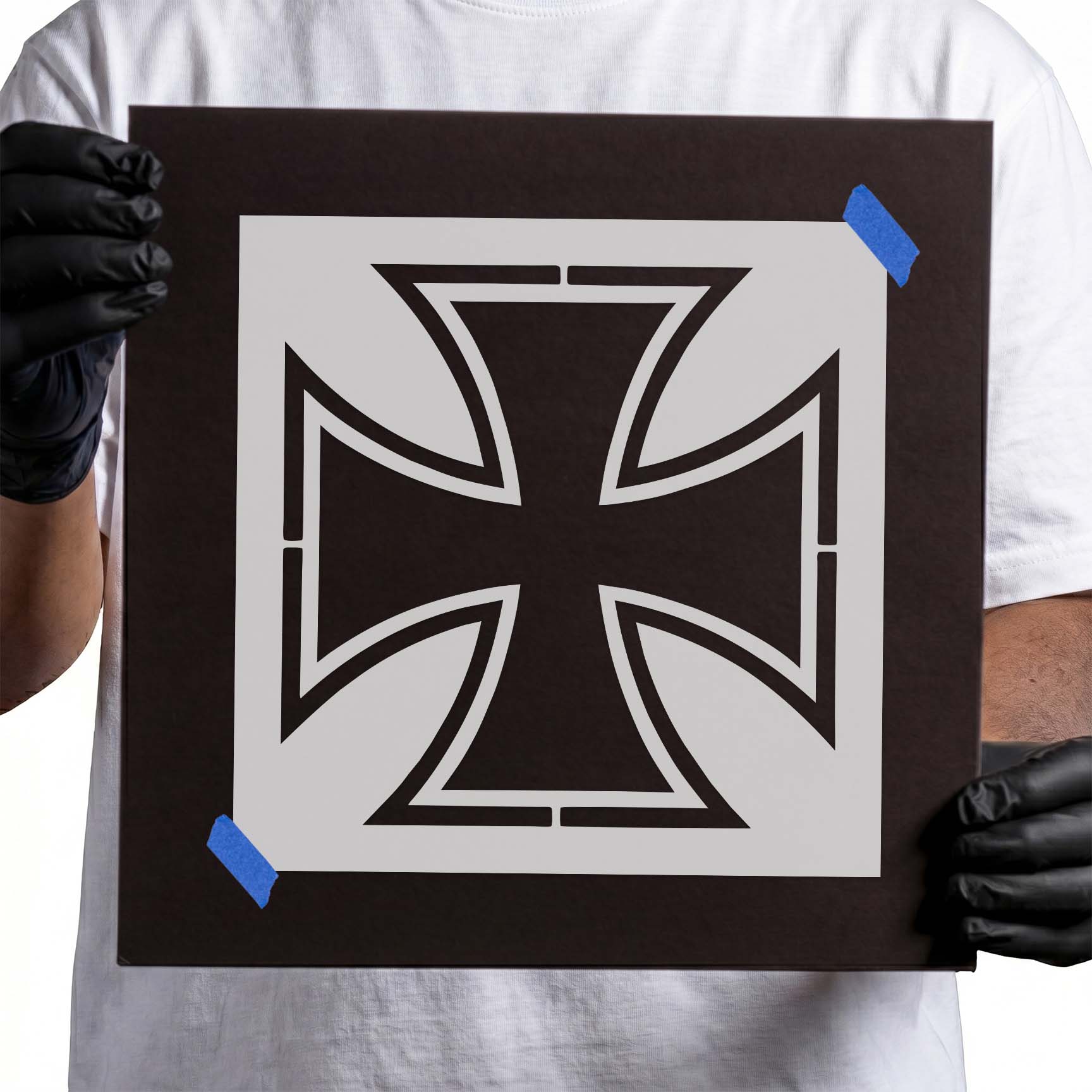 Person holding Iron Cross Stencil taped to black cardboard
