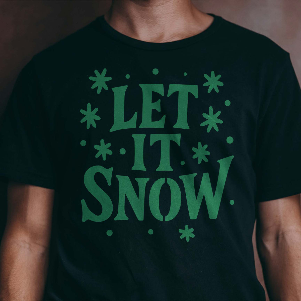 Green Let It Snow Hand Lettered Stencil adds playful snowflakes across a black T-shirt.