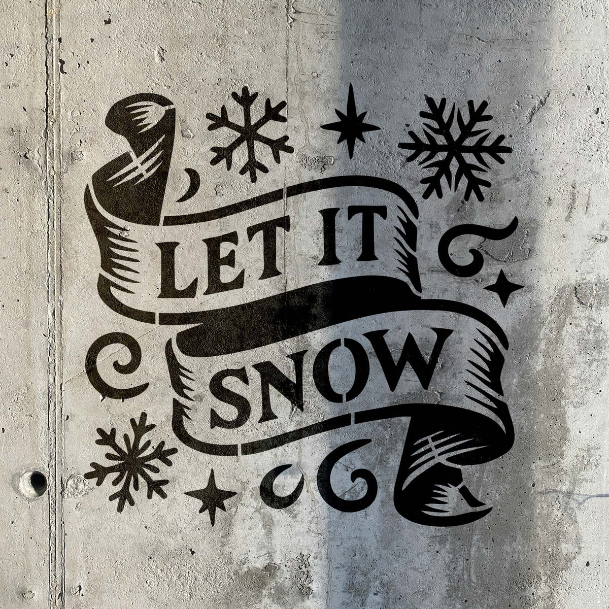 Let It Snow Banner Stencil pairs flowing ribbon text with snowflakes on a weathered concrete wall.