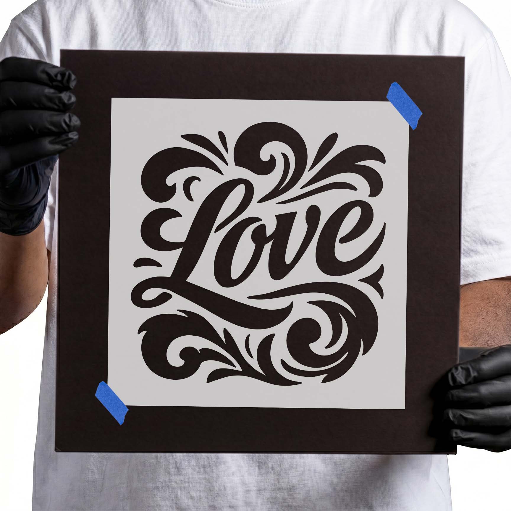 Gloved hands holding Love Script with Flourishes Stencil taped to cardboard