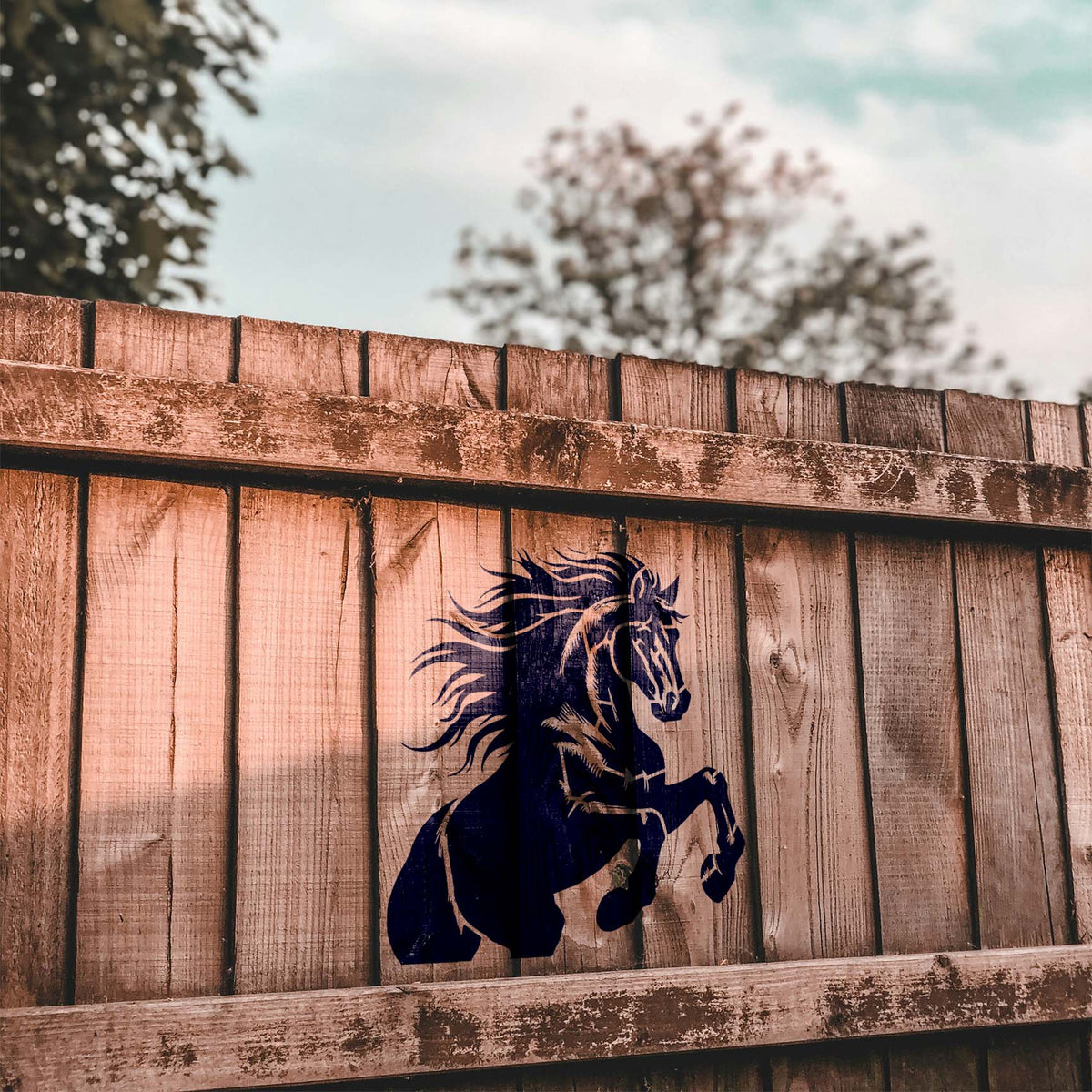 A rustic wood fence features the Majestic Rearing Stallion Stencil with its mane flowing and front legs raised.
