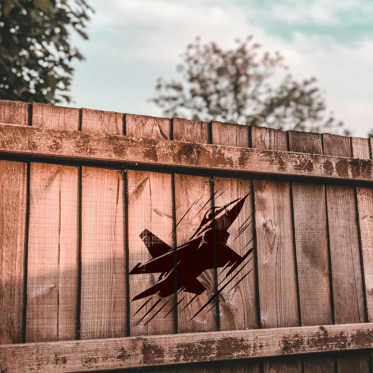 Modern Fighter Jet Silhouette Stencil displayed in dark paint on a rustic wood fence