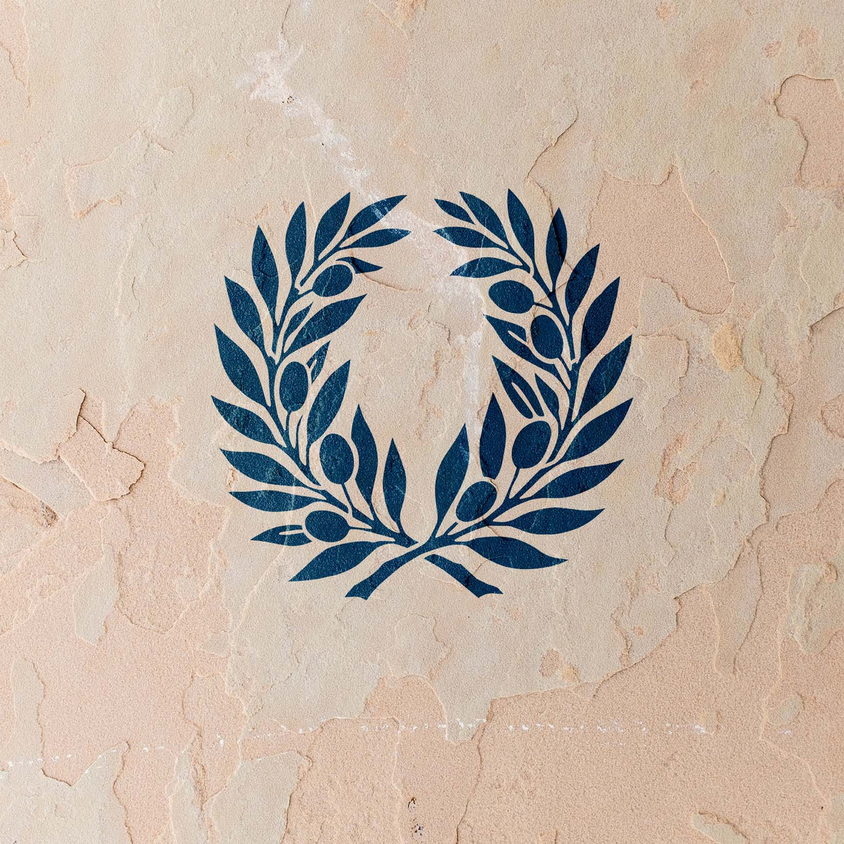 Two olive branches form the Olive Branch Wreath Stencil in rich blue against a weathered stucco wall.