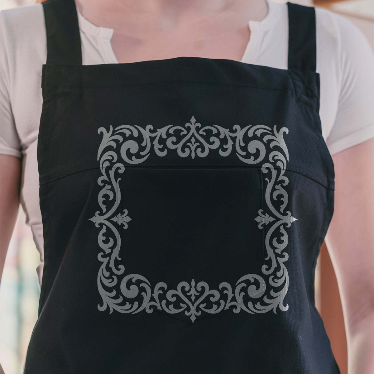 Silver Ornate Gothic Filigree Border Stencil decorates the front of a black apron