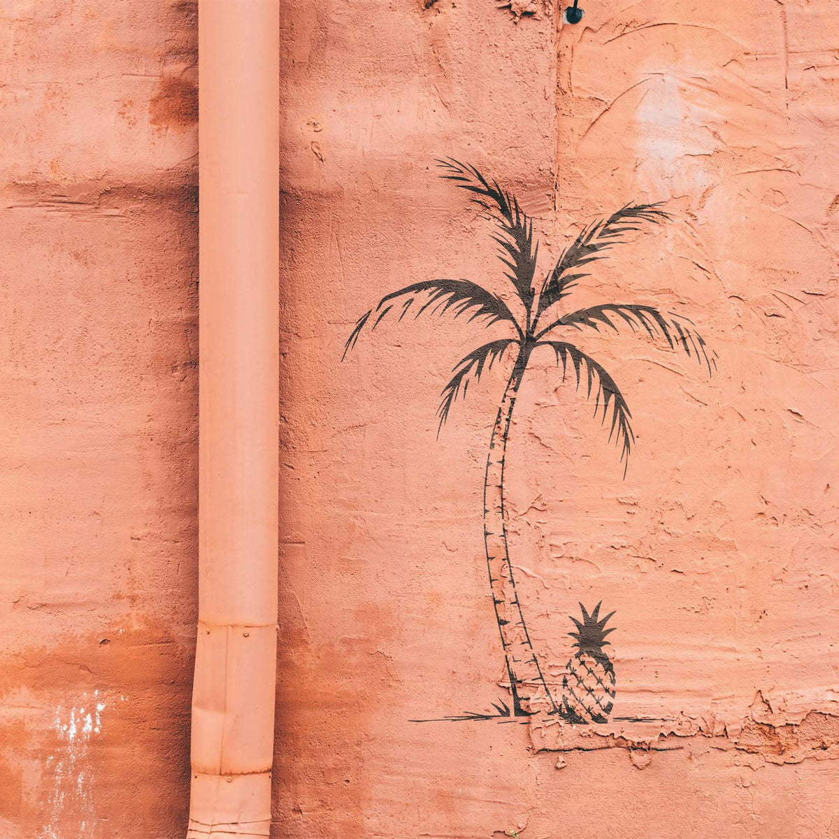 Tropical Palm & Pineapple Stencil shows a curved palm tree and pineapple painted on a textured peach wall