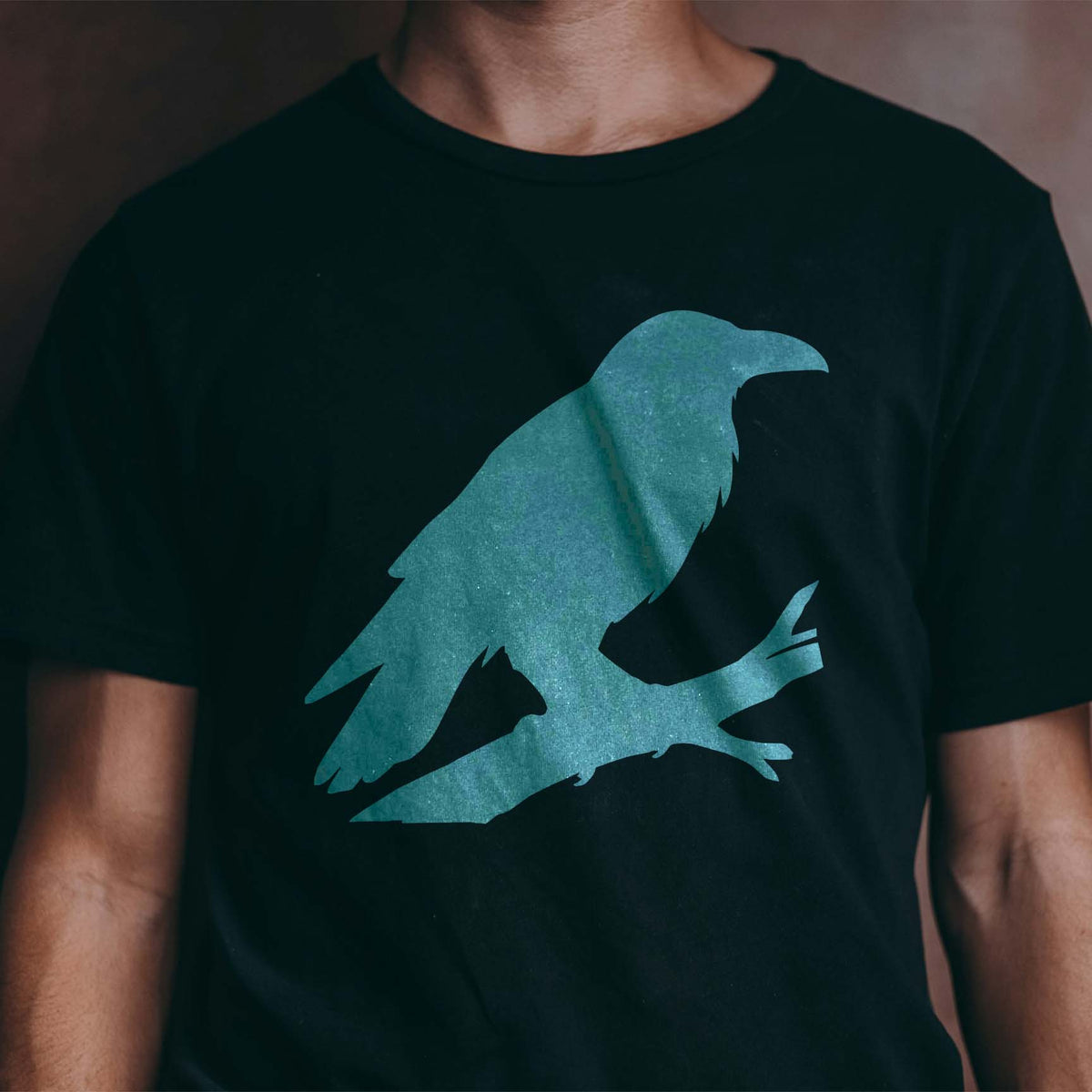 Perched Raven Stencil featured on a black T-shirt with a large blue raven resting on a branch.