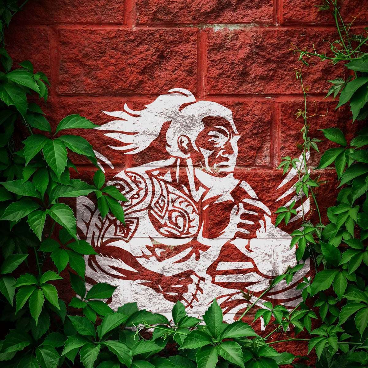 Polynesian Warrior Stencil painted white on an ivy-covered red brick wall.