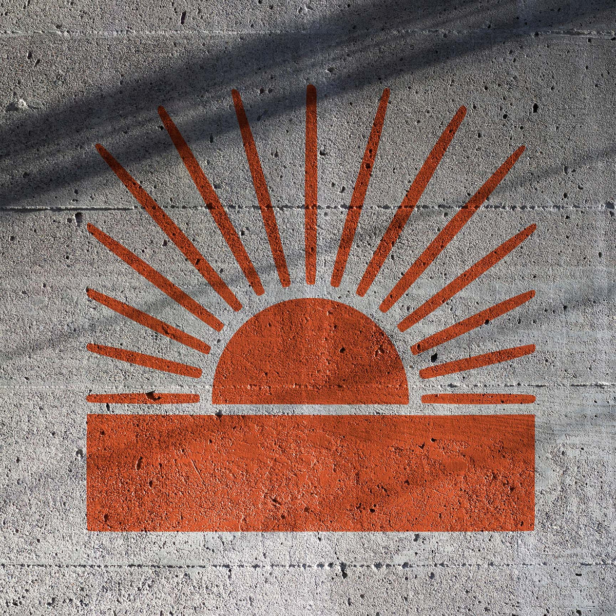 A textured concrete wall features the Radiant Sunrise Horizon Stencil in warm orange with striking sunrays.