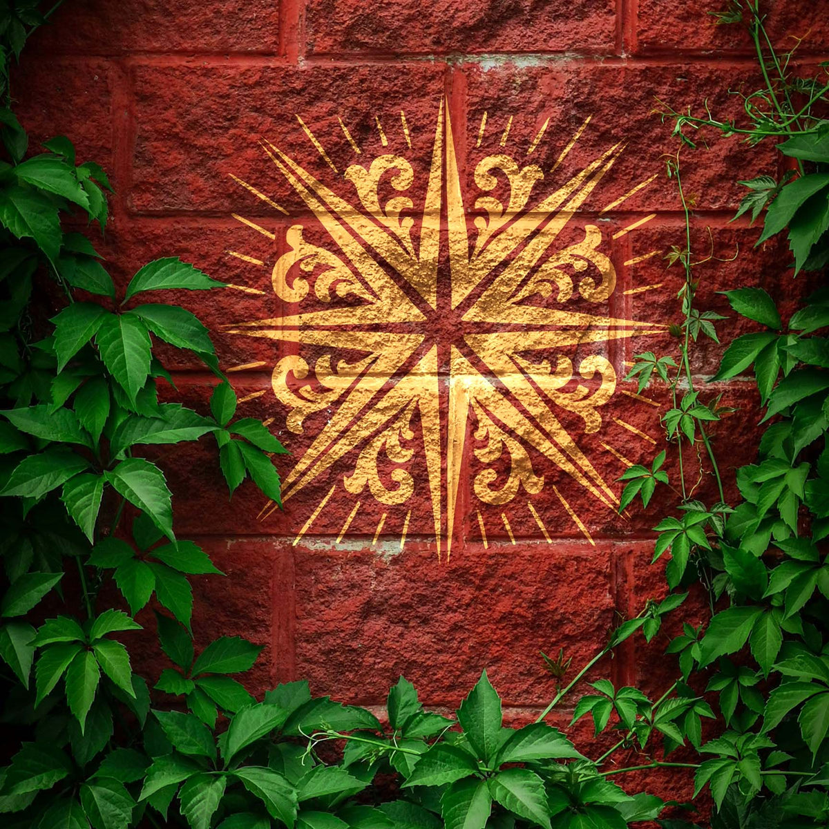 Among leafy vines, a gold Radiating Scroll Star Stencil shines against a red brick wall