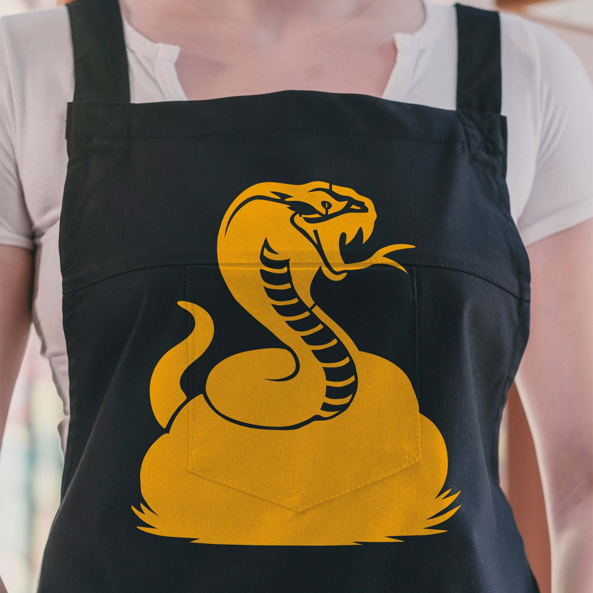 Golden Raised Cobra Stencil coils with fangs and tongue across a black apron