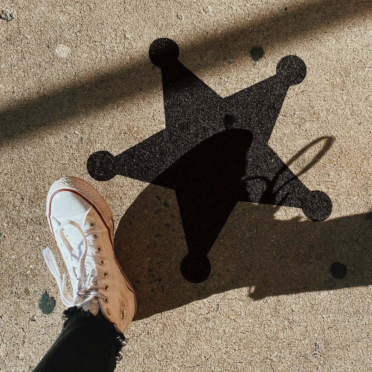 Under dramatic outdoor shadows, the Sheriff Star Stencil stands out on textured concrete