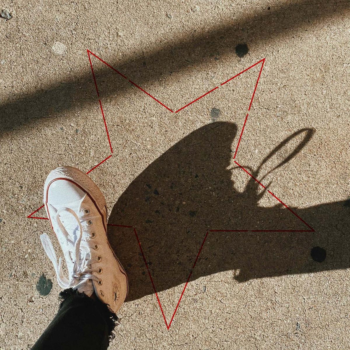 Sunlight and bold shadows frame the Simple Outline Star Stencil painted on textured pavement